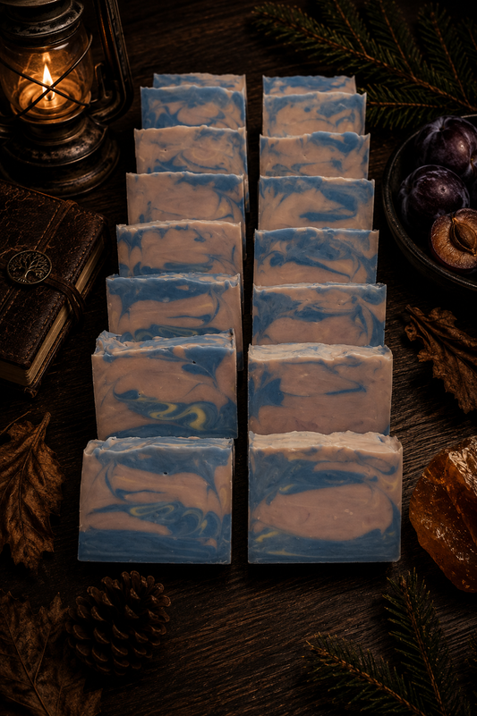 Stack of soap bars with blue and lavender swirls on a dark surface with a candle and fruit in the background.